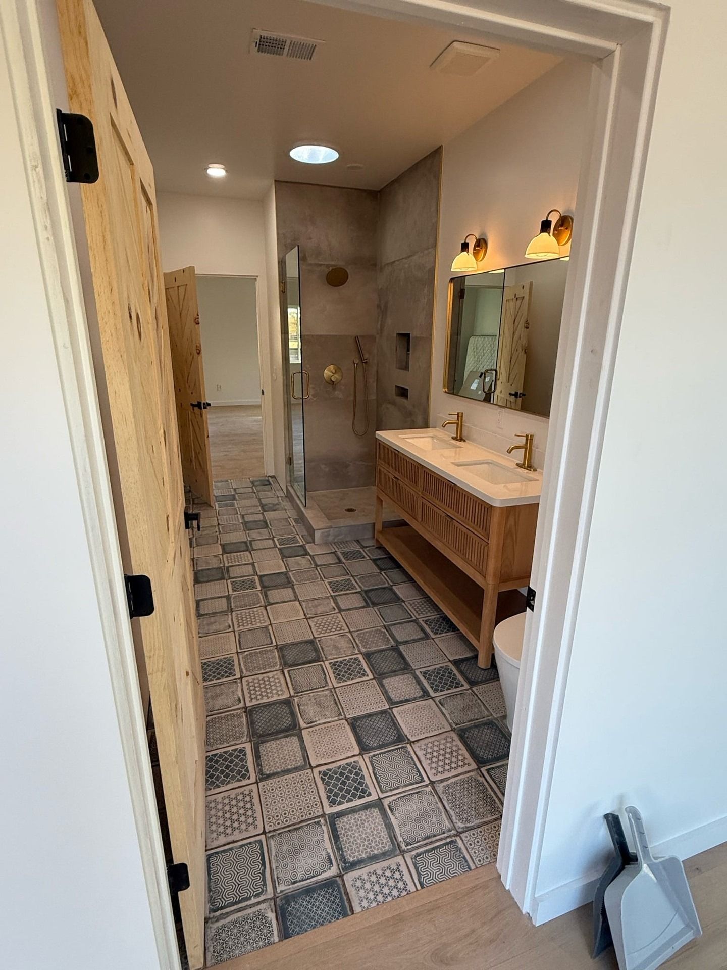 Narrow bathroom hallway with patterned tile floor, wood vanity, mirror, and shower stall in the back.