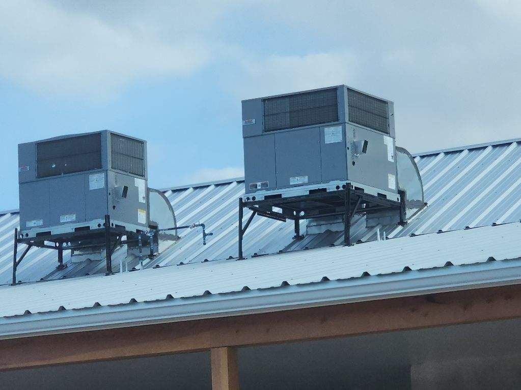 Two HVAC units on a metal rooftop under a cloudy sky