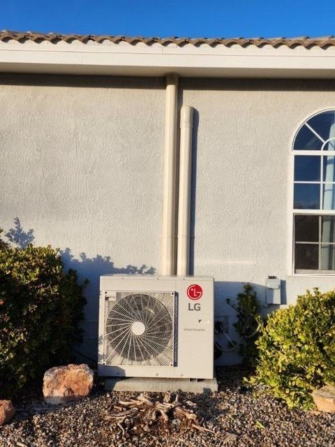 Outdoor LG air conditioning unit beside a stucco house wall and bushes.