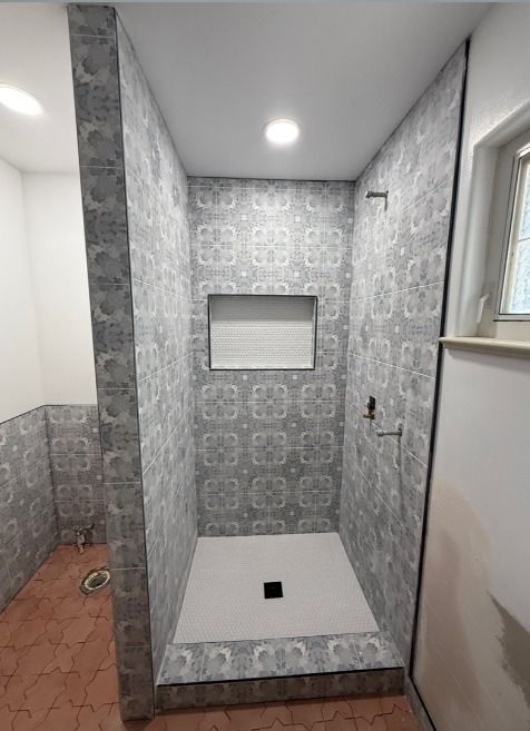 Tiled walk-in shower with recessed shelf, ceiling light, and small floor drain in a gray bathroom