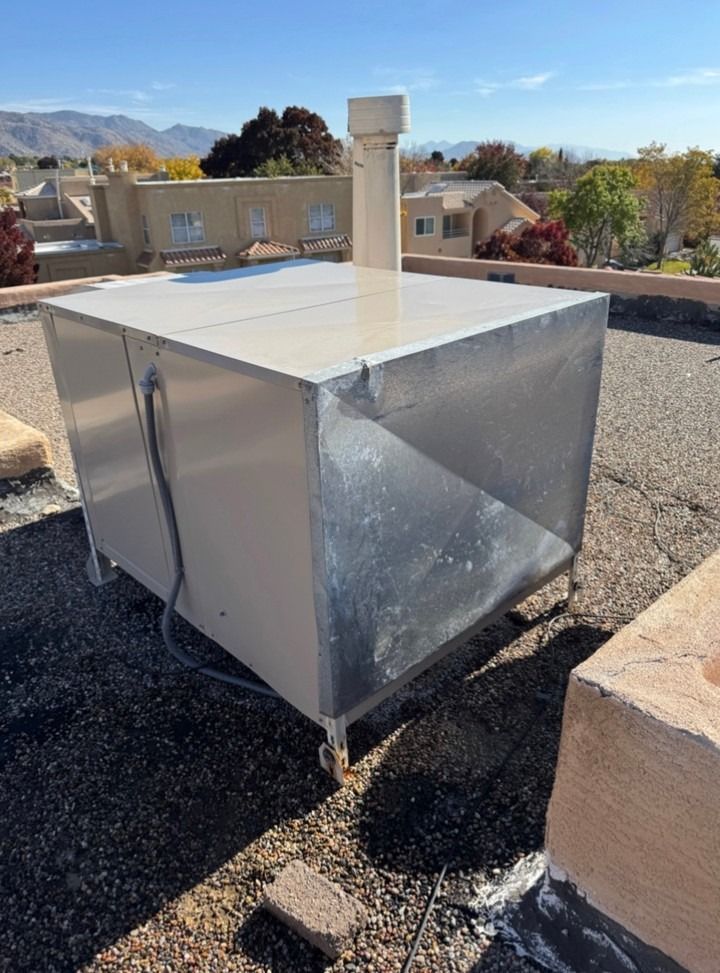 Metal rooftop HVAC unit with a white vent pipe under a clear sky