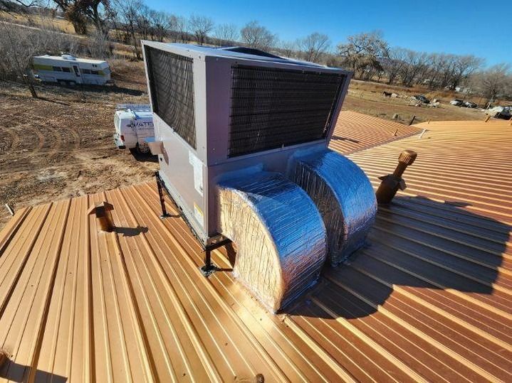 Roof-mounted HVAC unit wrapped in blue insulation on a corrugated metal roof under a clear sky