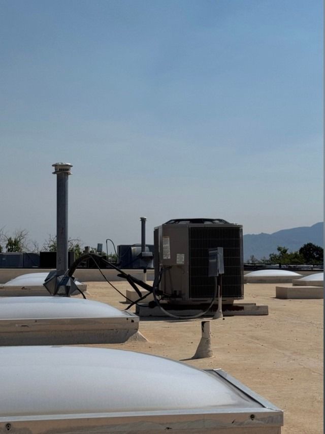 Rooftop HVAC units and vents on a flat beige roof under a clear blue sky