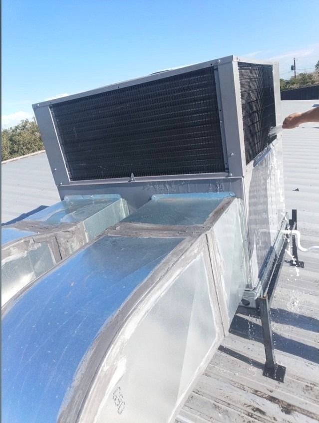 Rooftop HVAC unit with shiny metal ductwork and a black vent panel under clear daylight