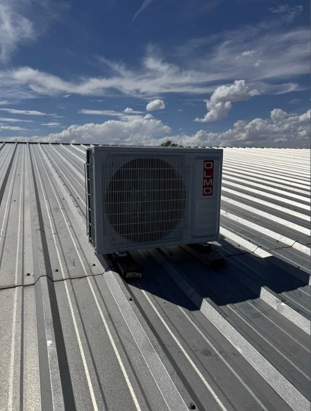 Rooftop HVAC unit on a corrugated metal roof under a blue sky with clouds