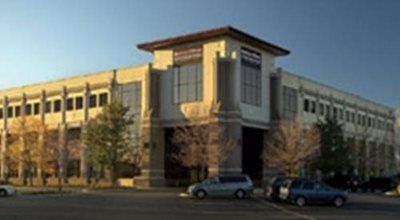 Office building with light-colored facade, brown roof, and arched entrance. Cars parked in front.