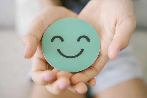 Hands holding a light green circle with a smiling face.