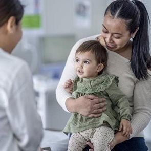 Woman holding a baby in a clinic, smiling at a doctor nearby.