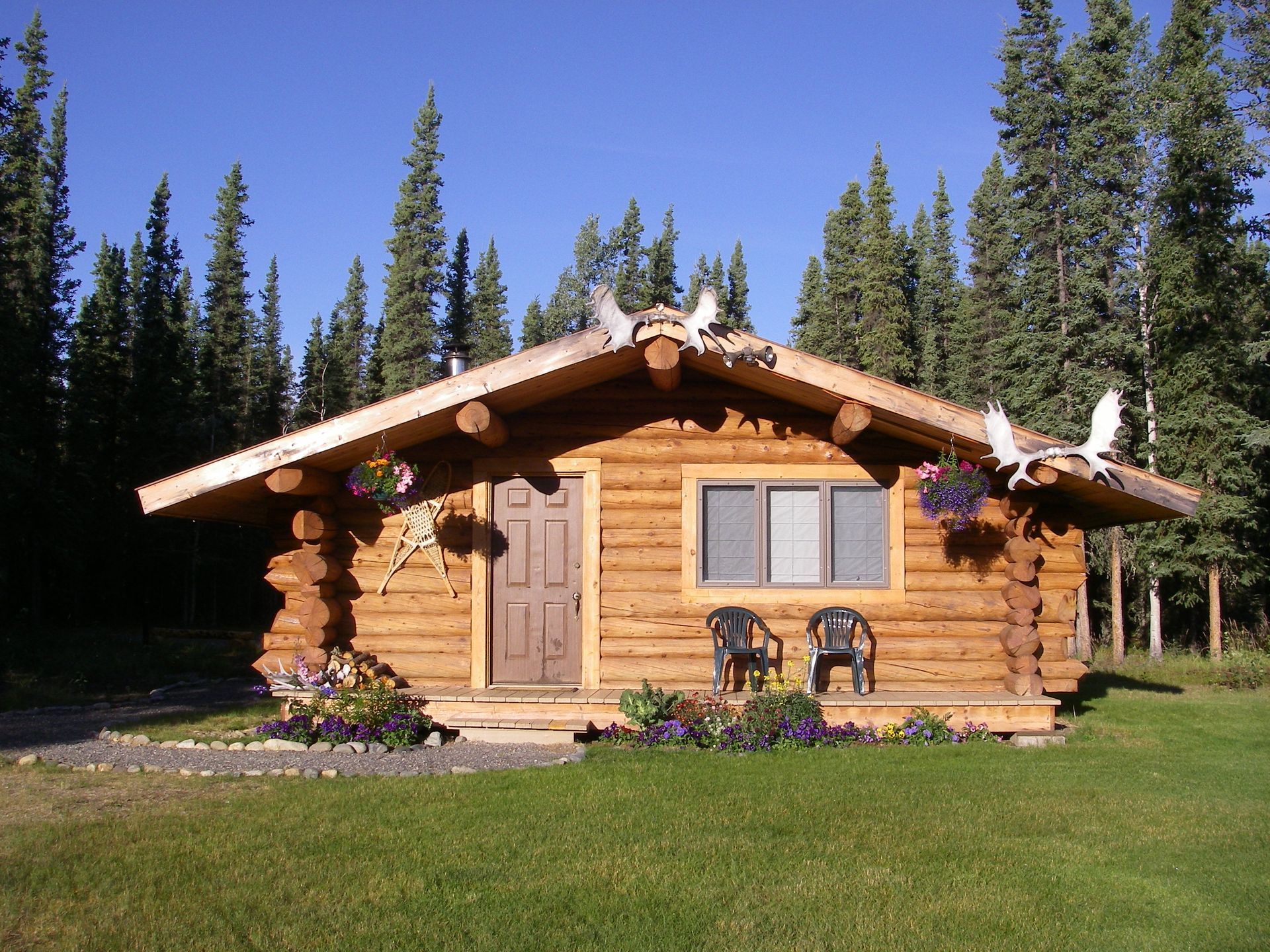 Log cabin with wooden exterior, window, door, and flowers on a grassy lawn.