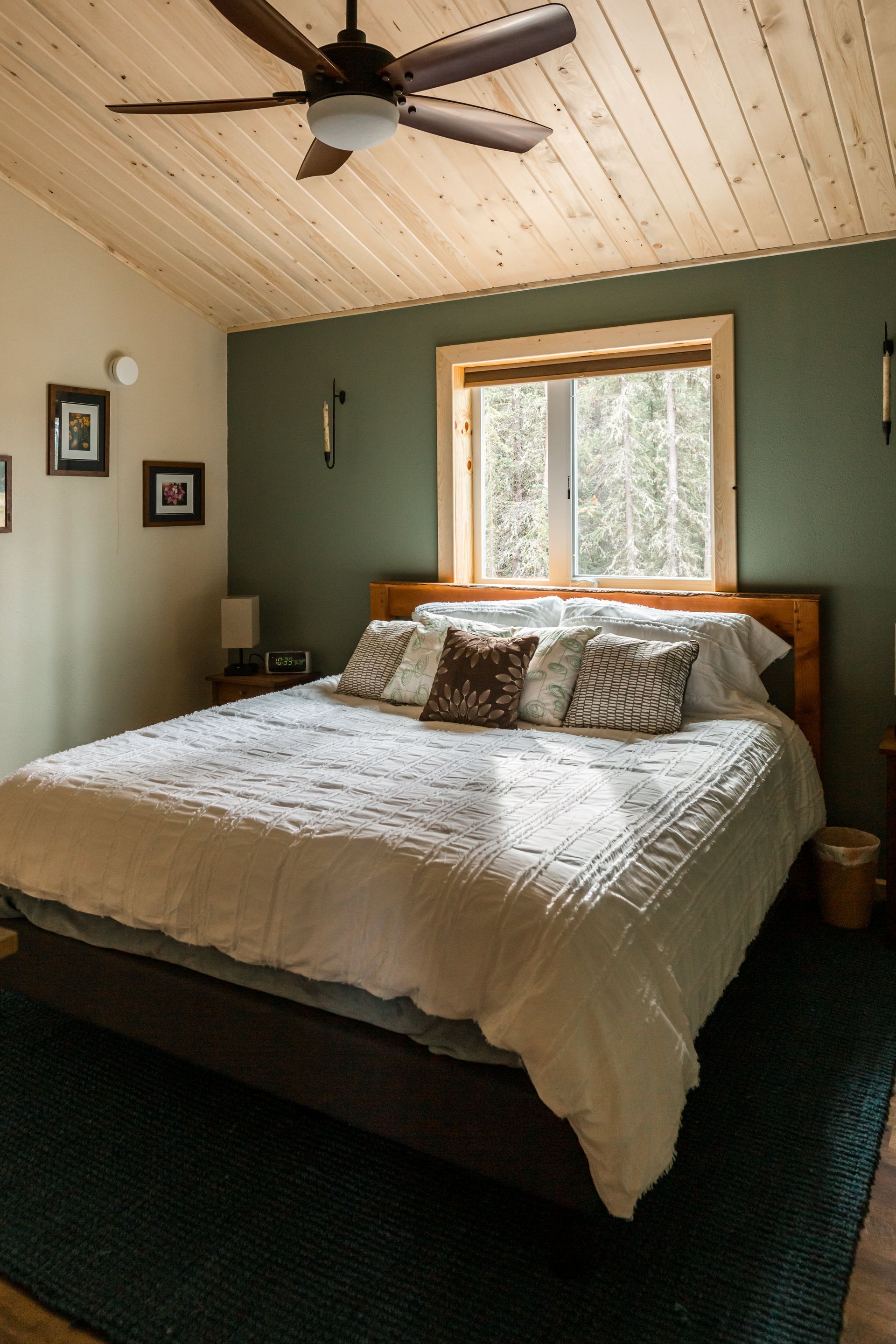 Bedroom with bed, green wall, and wooden ceiling. Sunlight streams through the window.