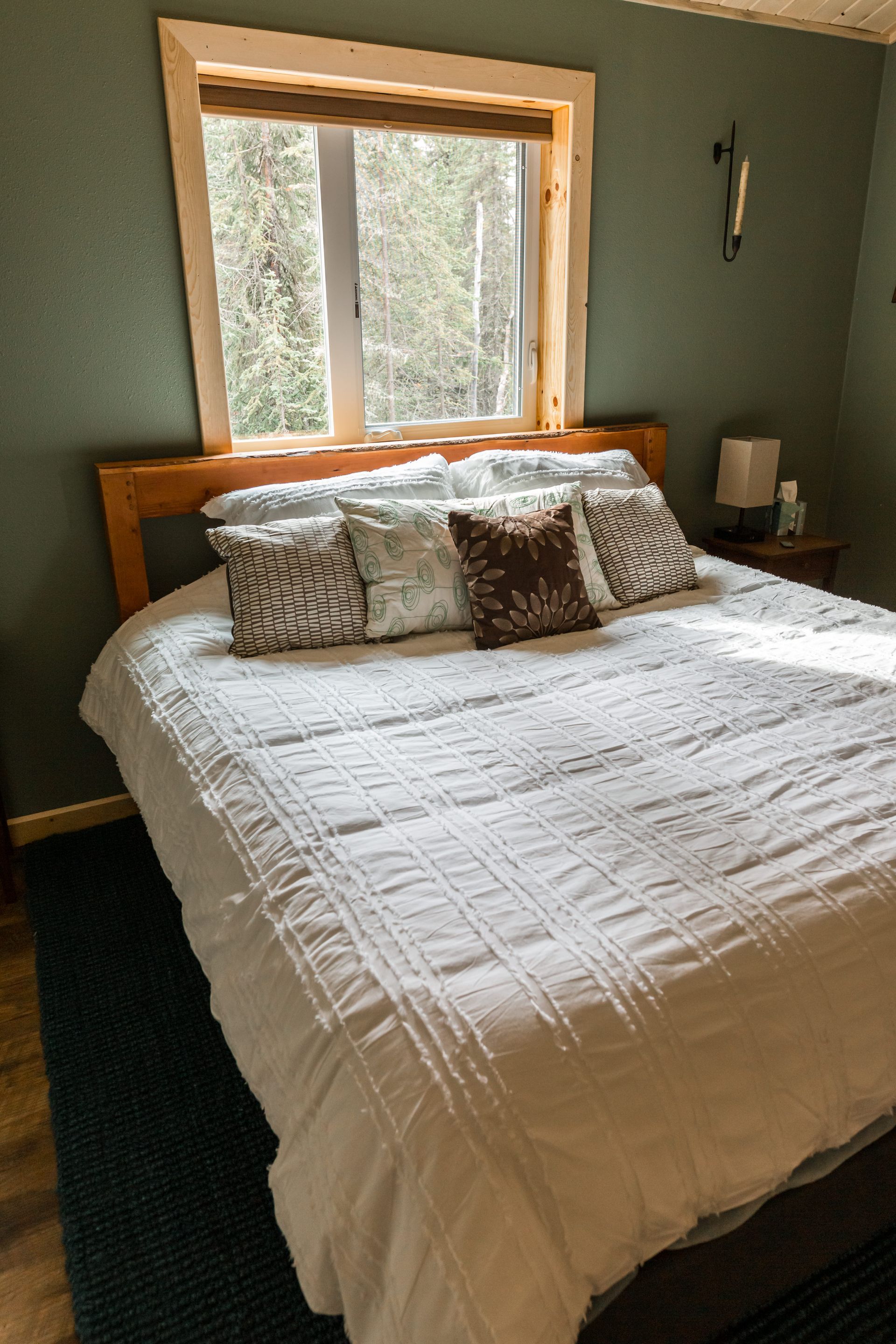 Bedroom with white bedding, pillows, and window above the bed. Dark green walls and rug.