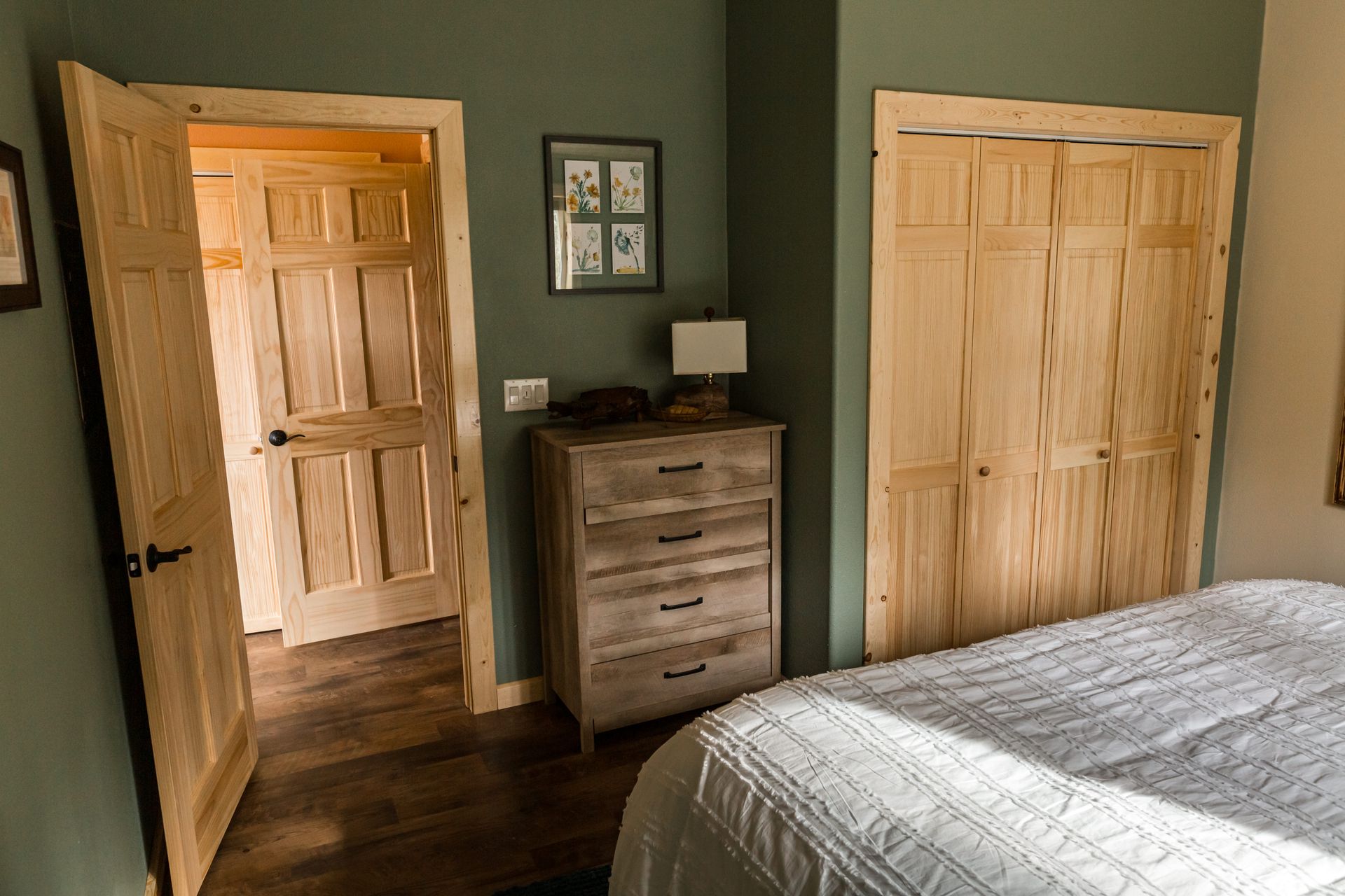 Bedroom with green walls, light wood doors, dresser, and closet. A bed is in the foreground.