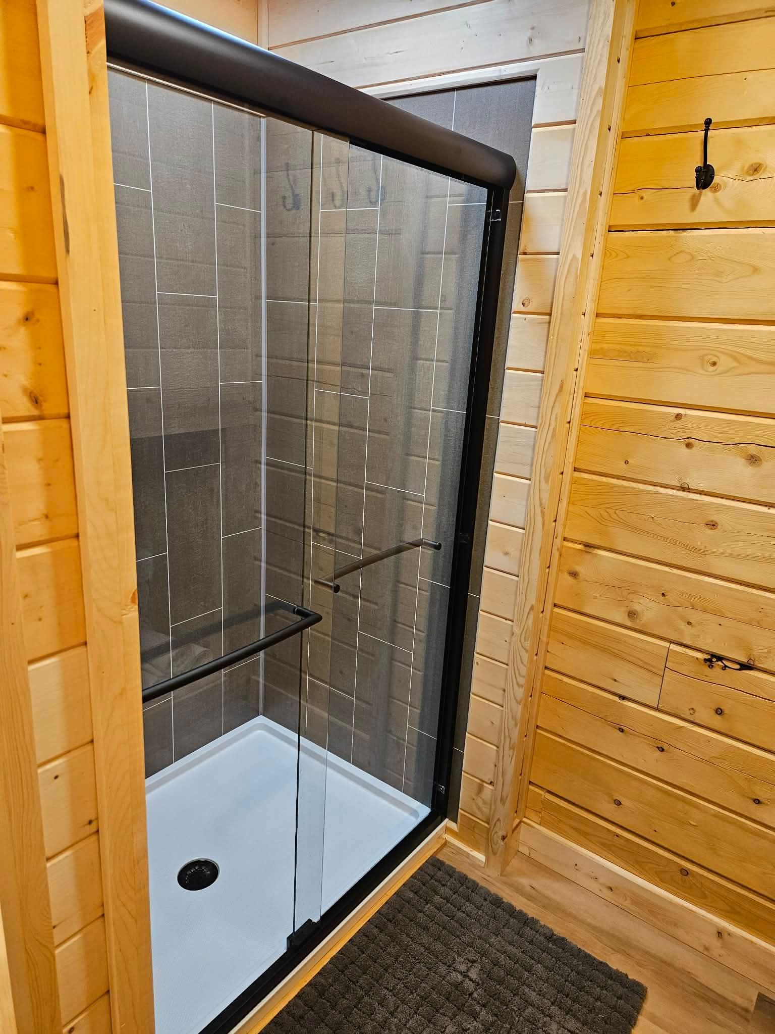 Glass shower enclosure in a wood-paneled bathroom with a black-and-white shower base.