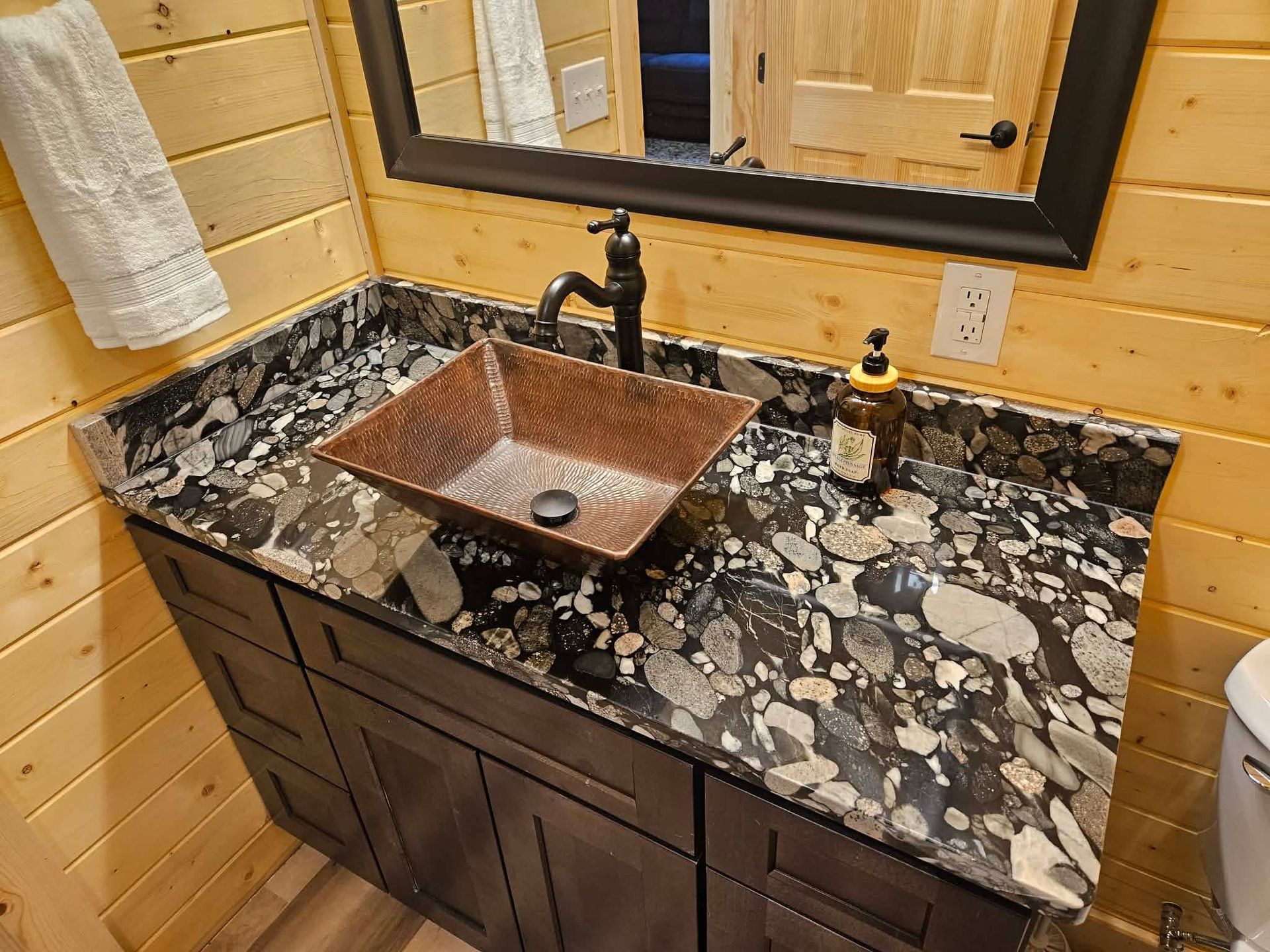 Rustic bathroom vanity with dark granite countertop, copper sink, and black faucet beneath a mirror.