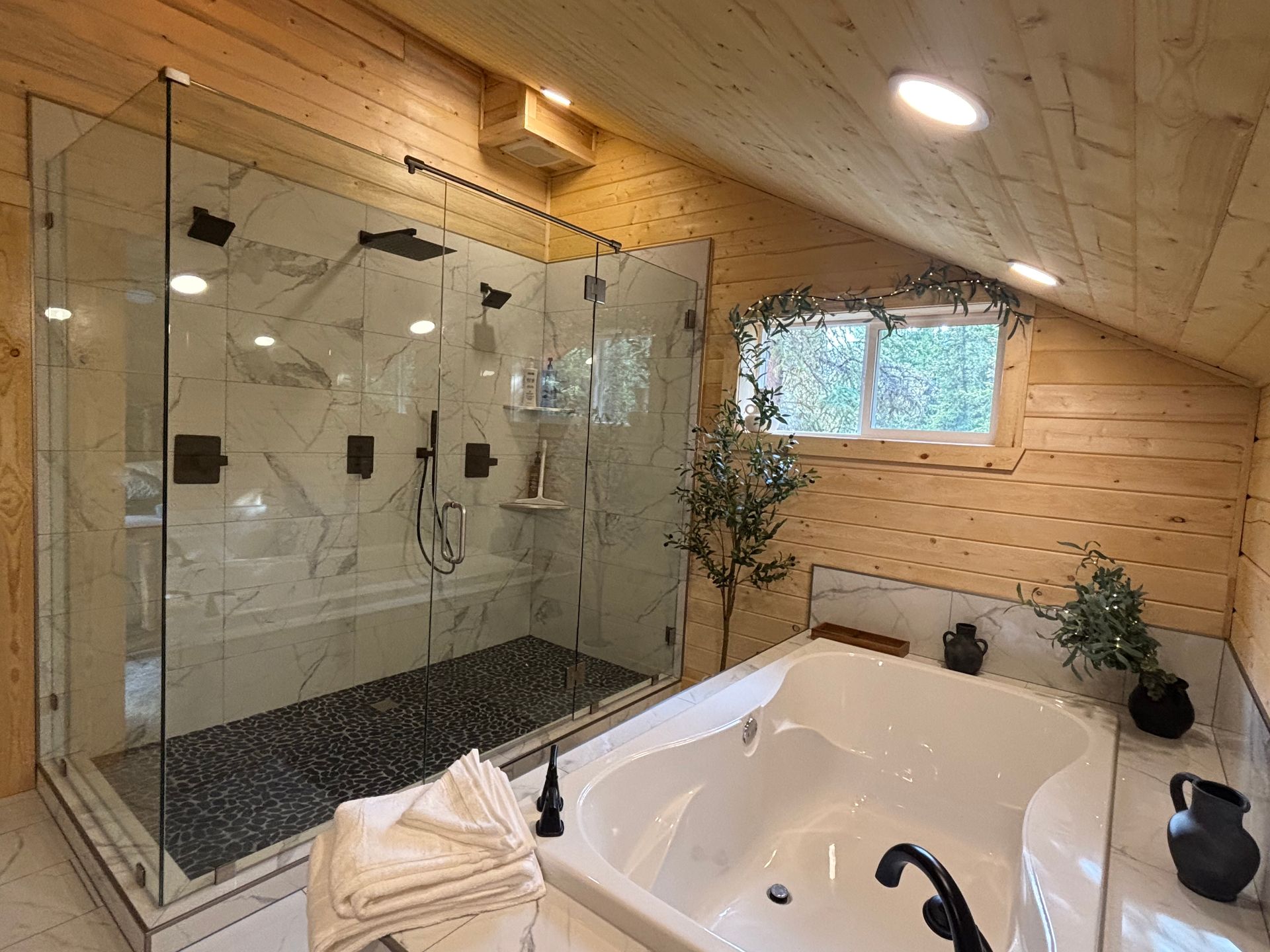 Luxury bathroom with glass shower, white soaking tub, and wood-paneled sloped ceiling