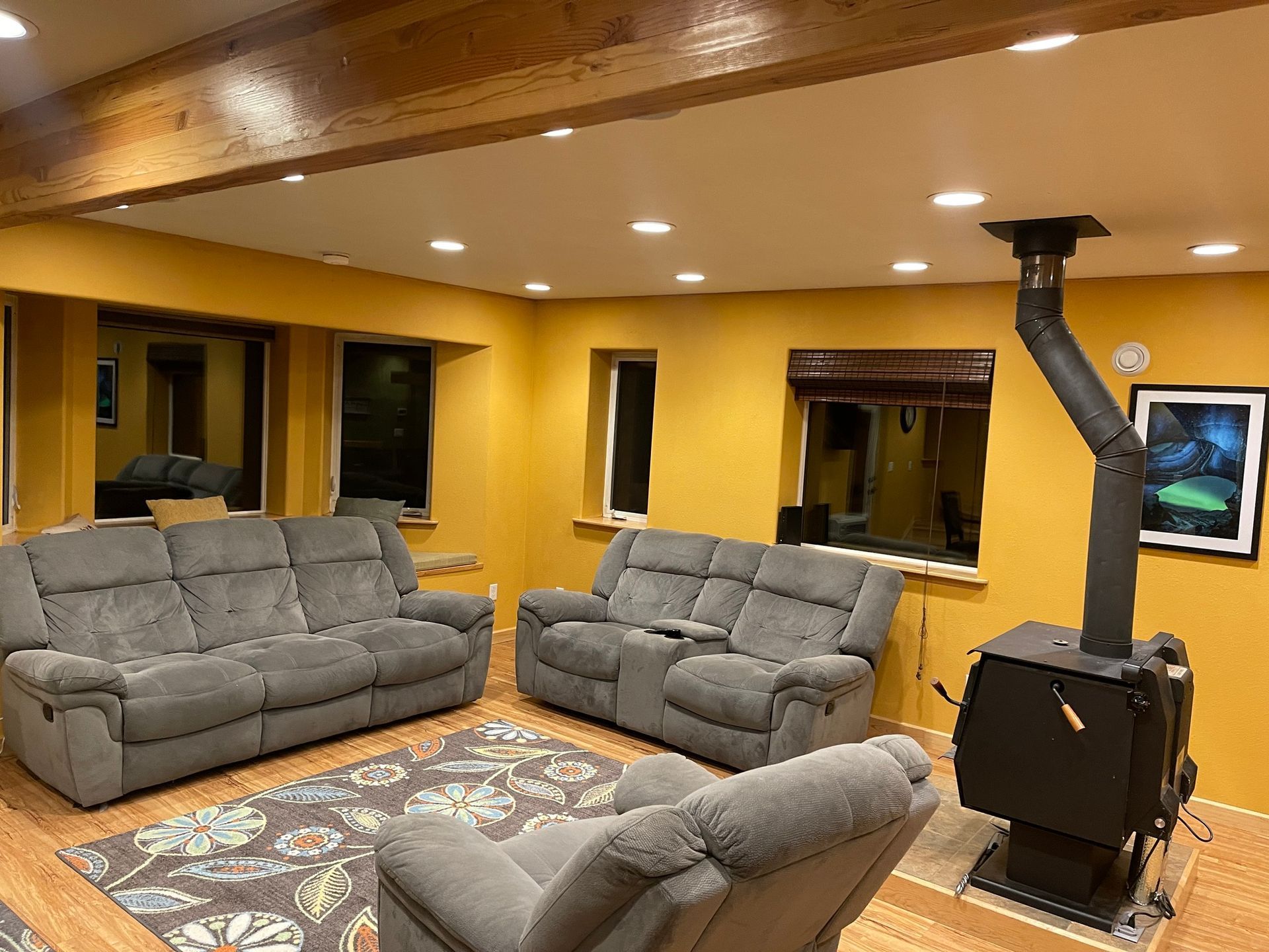 Cozy living room with gray reclining couches, wood-burning stove, rug, and yellow walls.