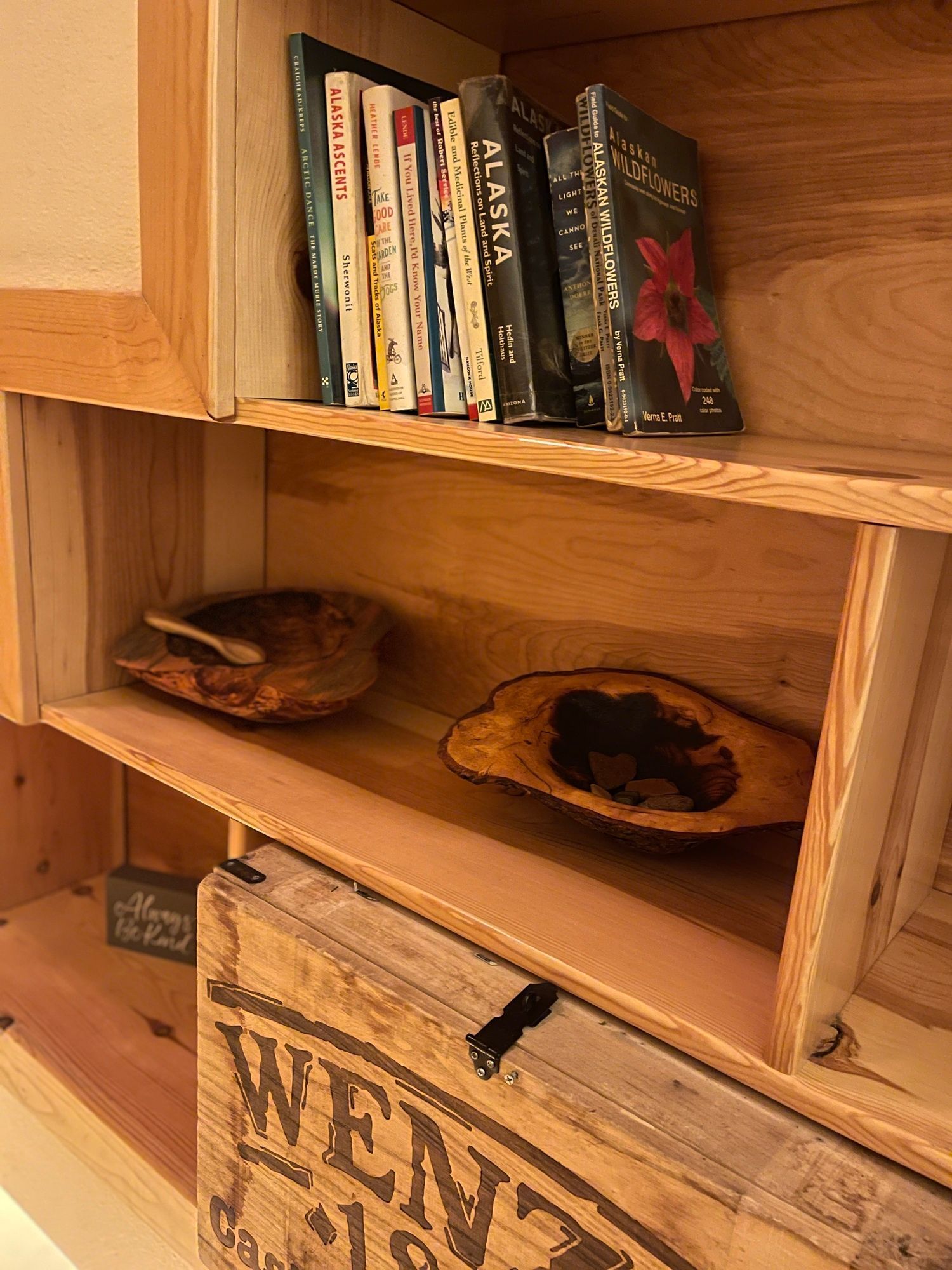 Wooden shelf with books and decorative wooden bowls. A wooden crate is visible at the bottom.