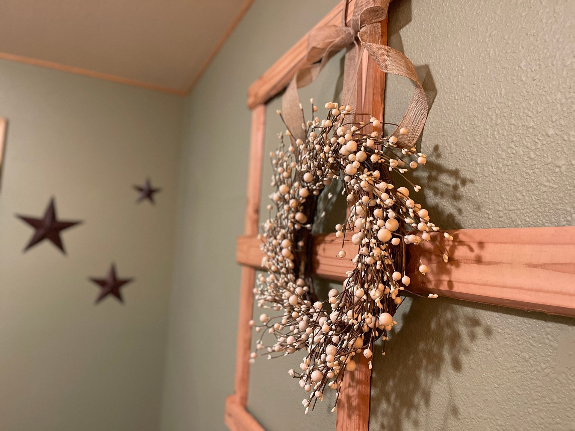 Wooden frame with berry wreath, tied with a ribbon, against a green wall with star decorations.