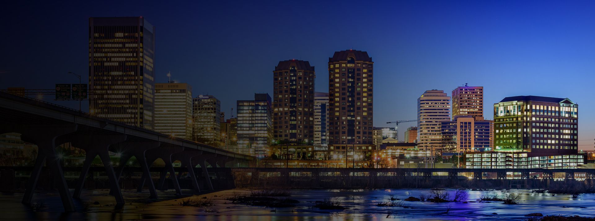 a city skyline at night with a bridge in the foreground .