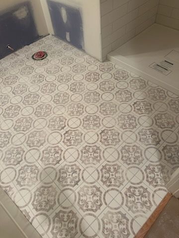 Bathroom floor with gray patterned tile, a drain, and a tiled shower corner