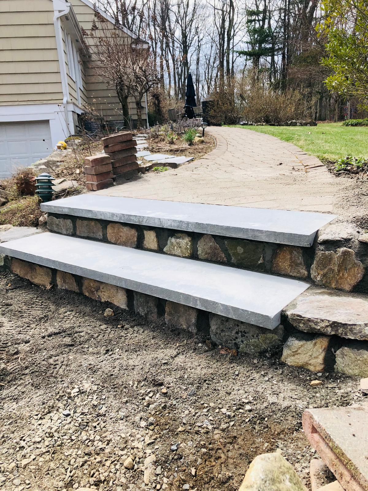 Stone retaining wall with concrete steps leading up a gravel driveway beside a house