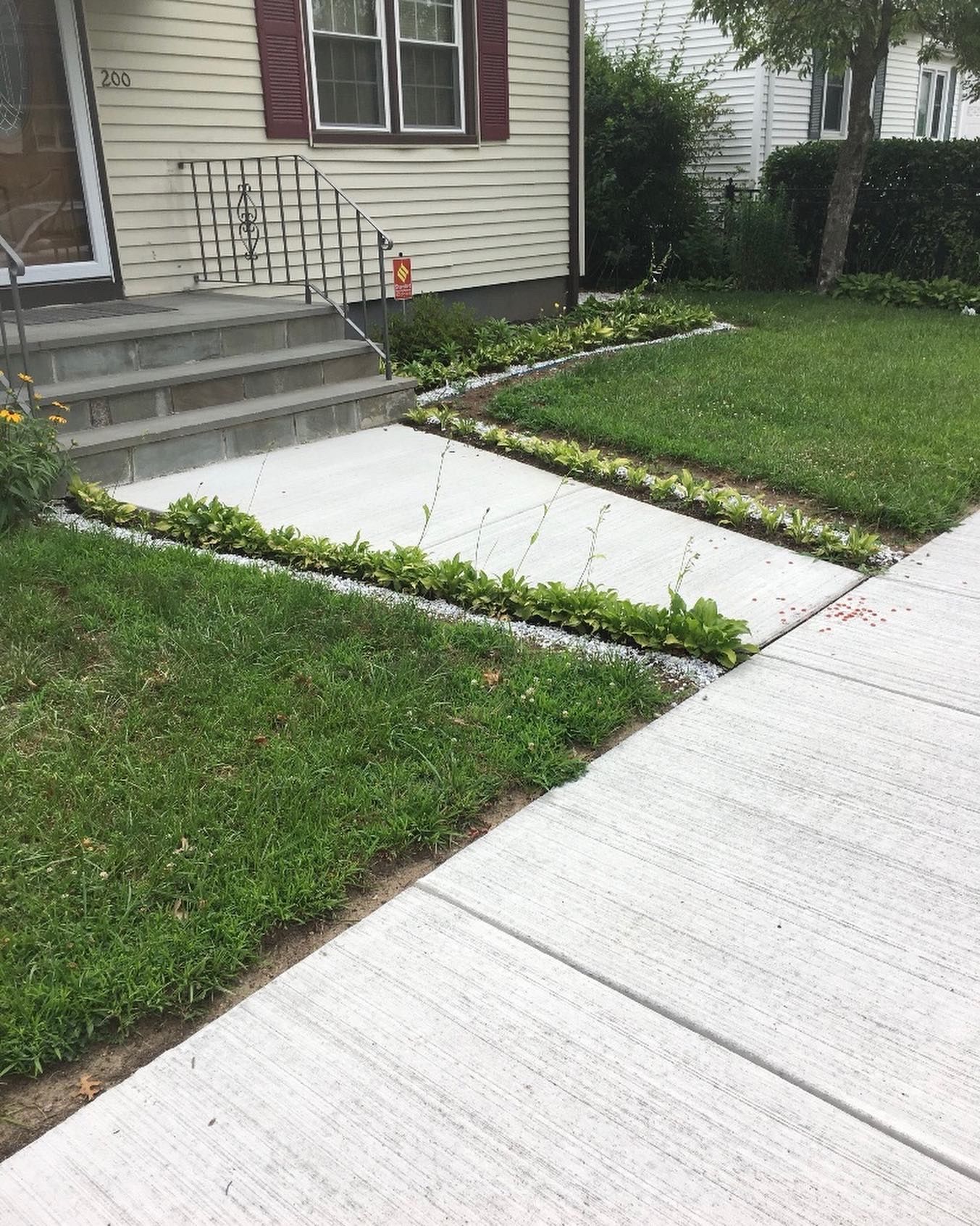 Front yard sidewalk and concrete walkway beside a house, bordered by grass and flower beds