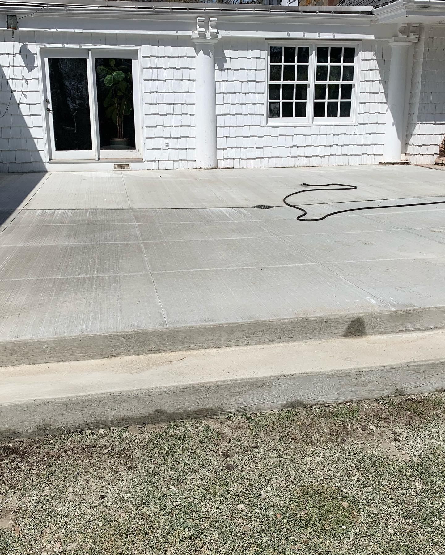Concrete patio in front of a white house with sliding glass doors and a window, with a hose on the ground