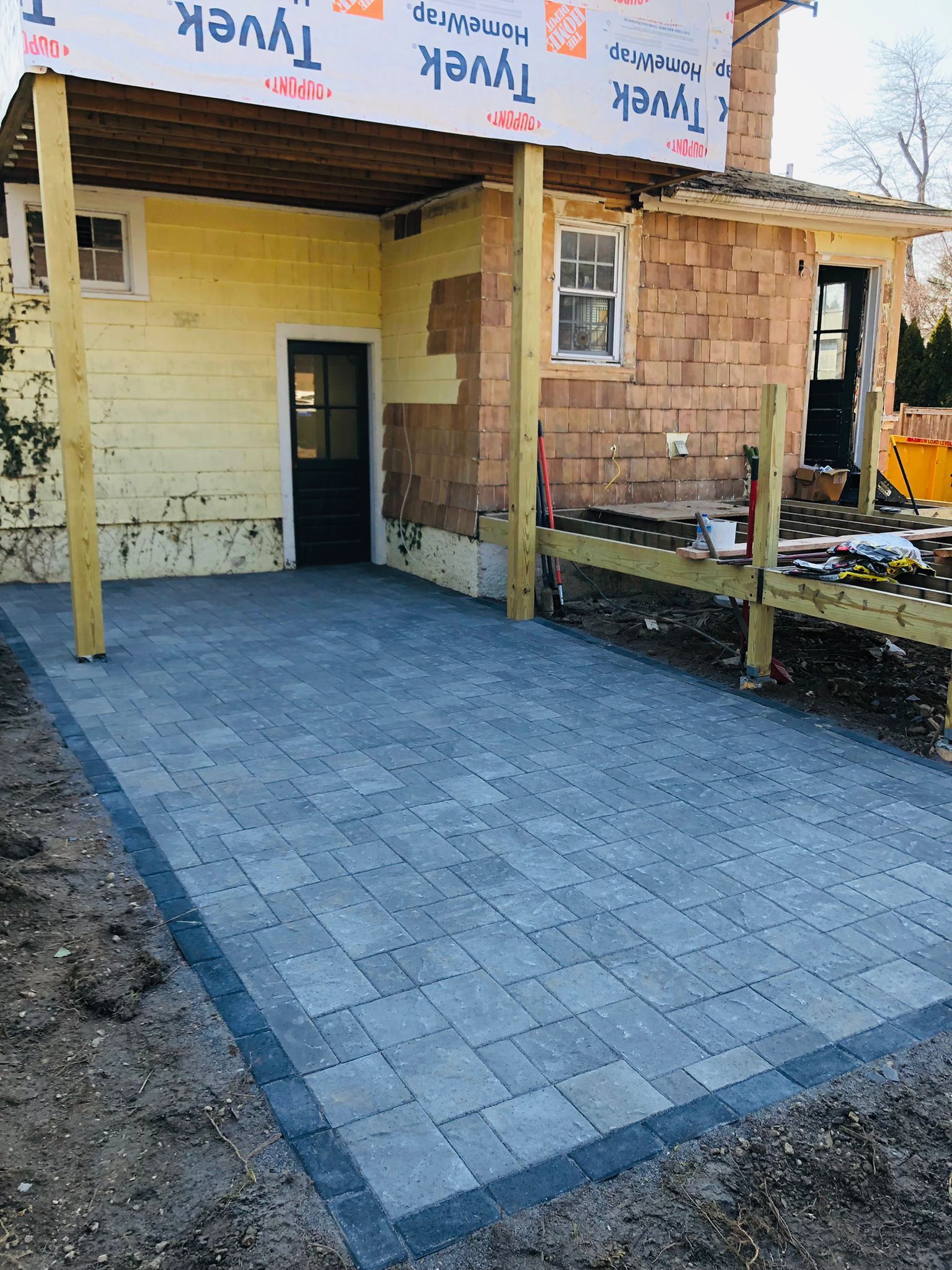 Paved front porch of a house under construction, with blue-gray pavers and unfinished walls.