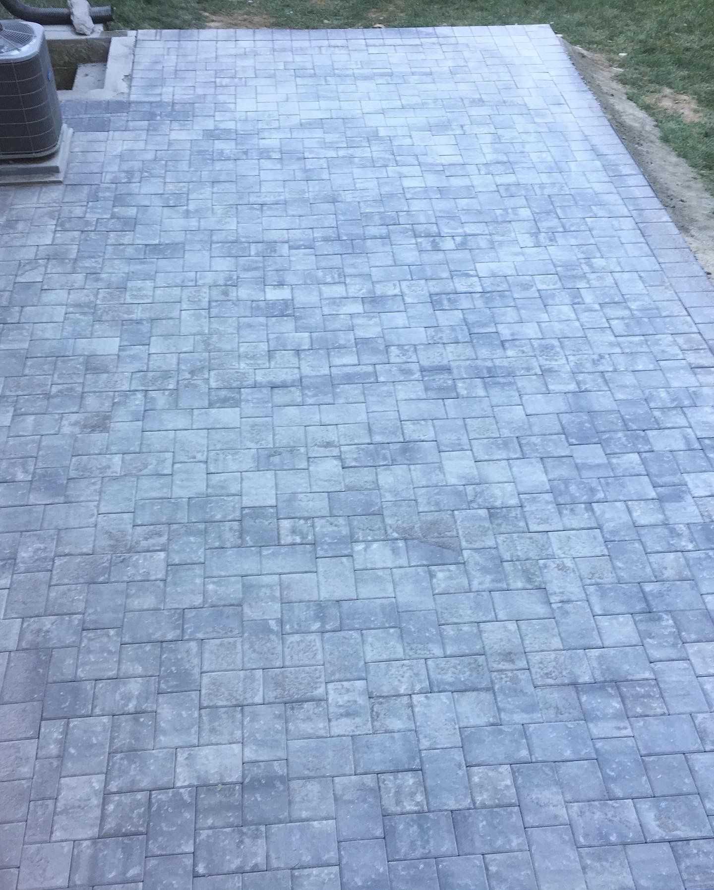 Gray stone paver patio or walkway with a neat rectangular pattern beside grass and a planter.