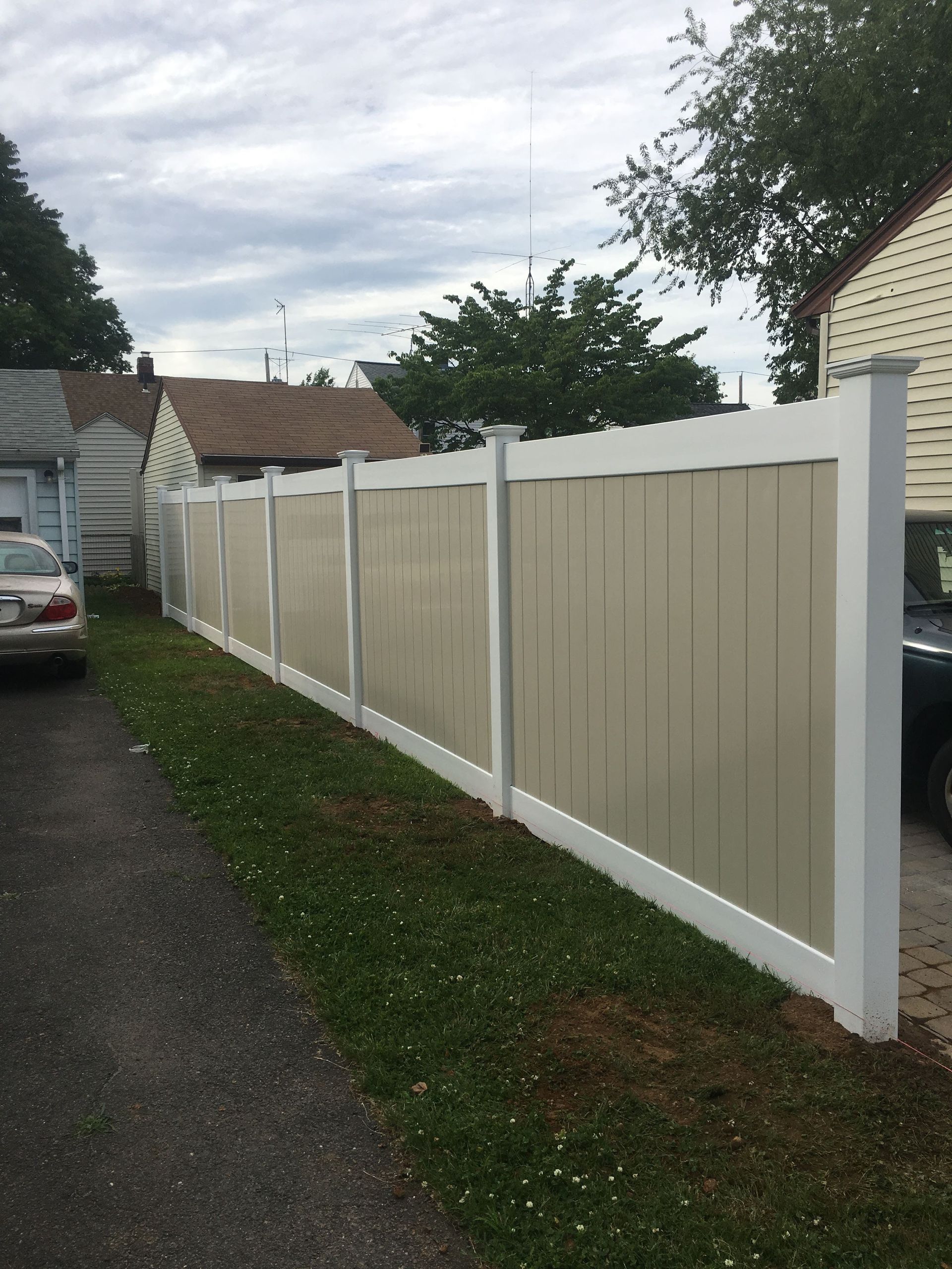 Beige and white vinyl fence along a narrow driveway beside a house under a cloudy sky
