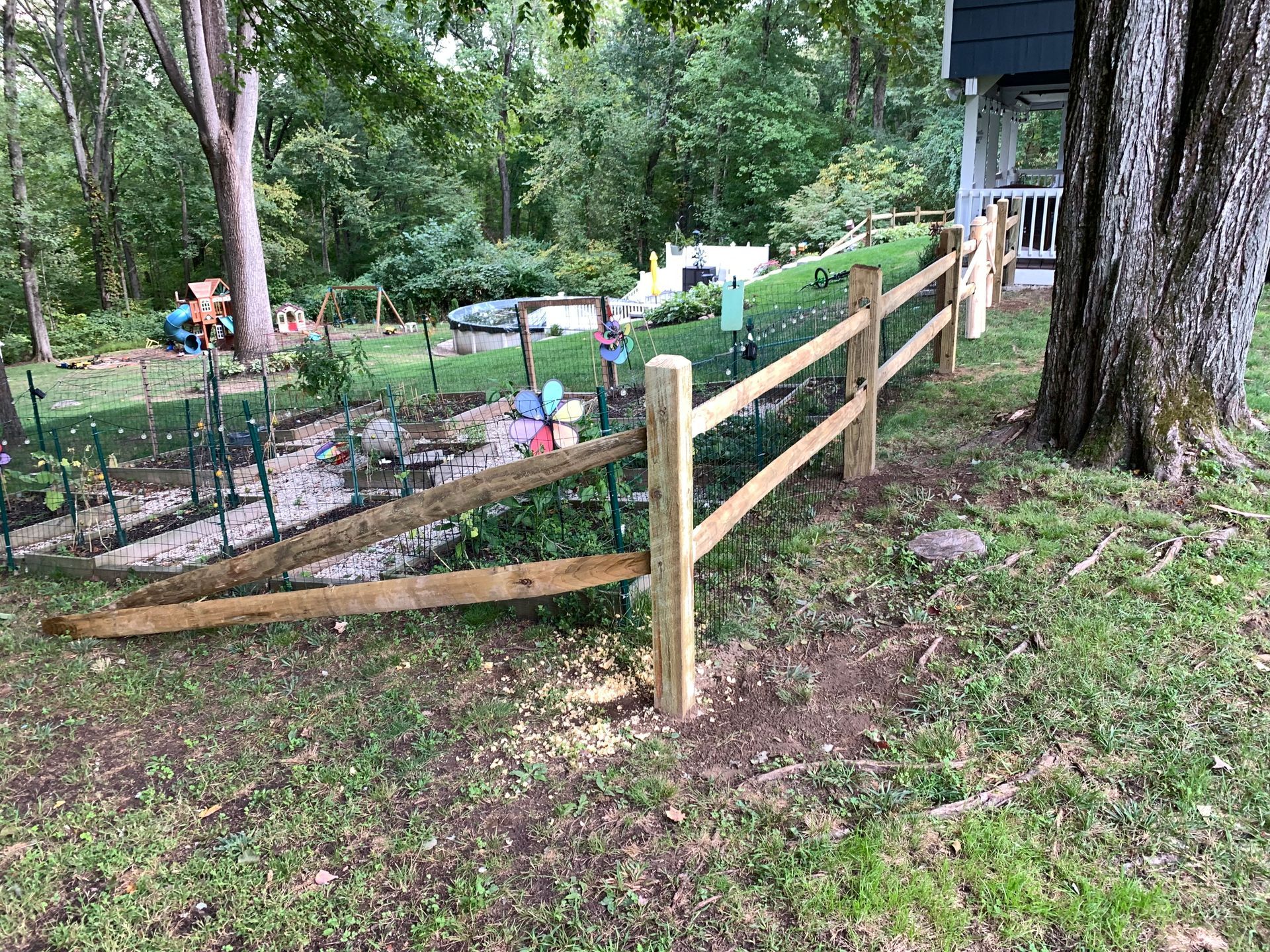Wooden fence bordering a garden area in a wooded yard beside a house.
