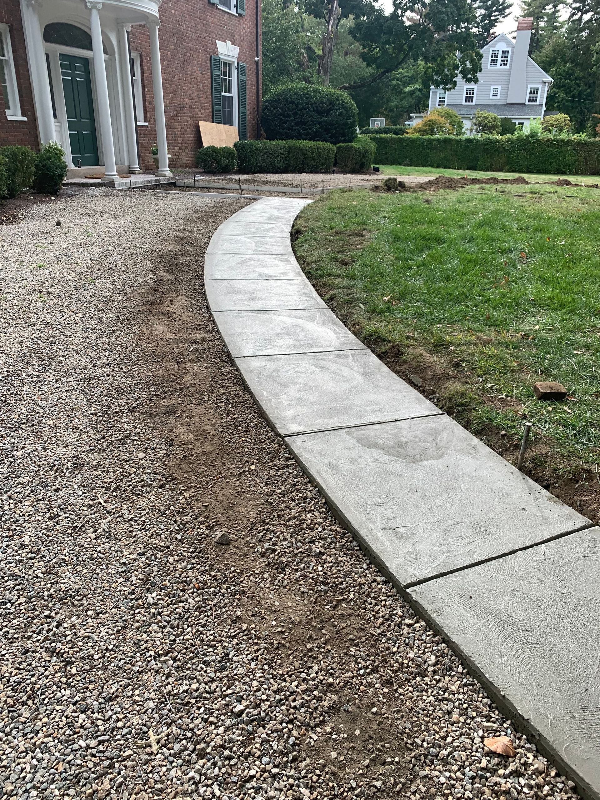 Curved concrete walkway beside a gravel path, green lawn, and brick building