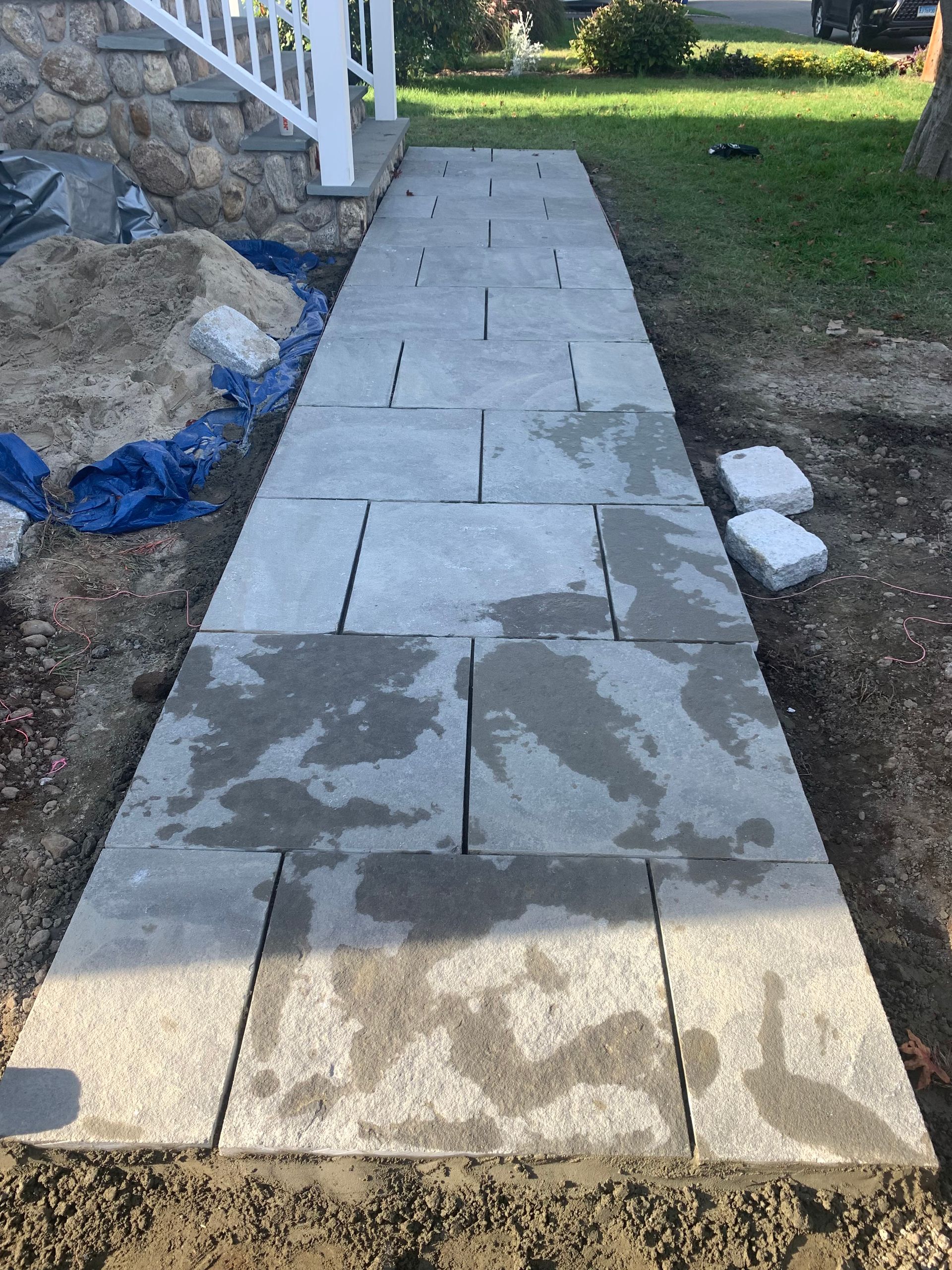 Concrete walkway beside a house, with wet patches and white edging stones in a yard.