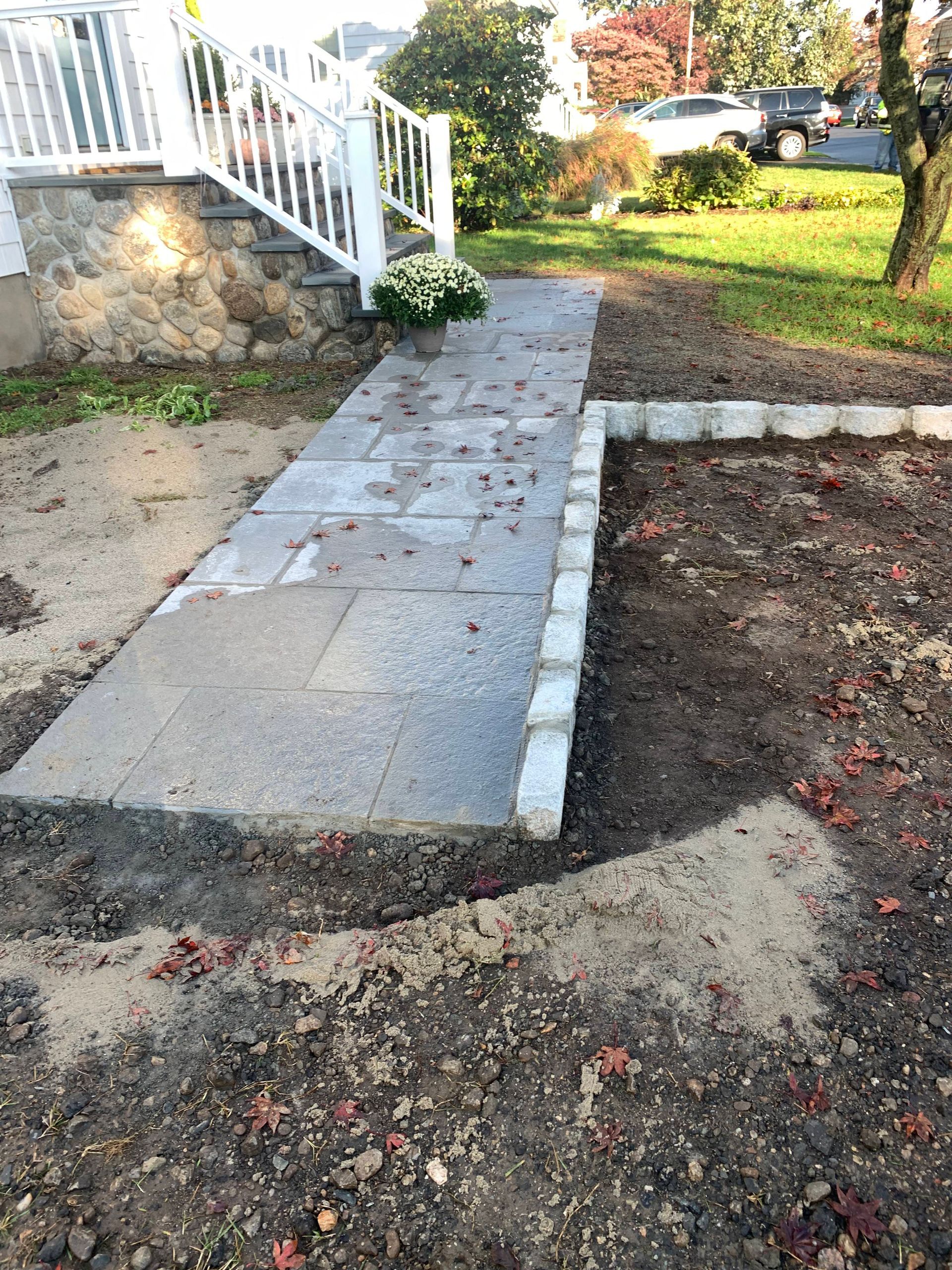 Stone walkway leading to a white porch beside a yard and garden bed