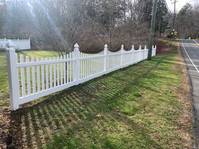White decorative picket fence along a grassy roadside beside a paved street in daylight