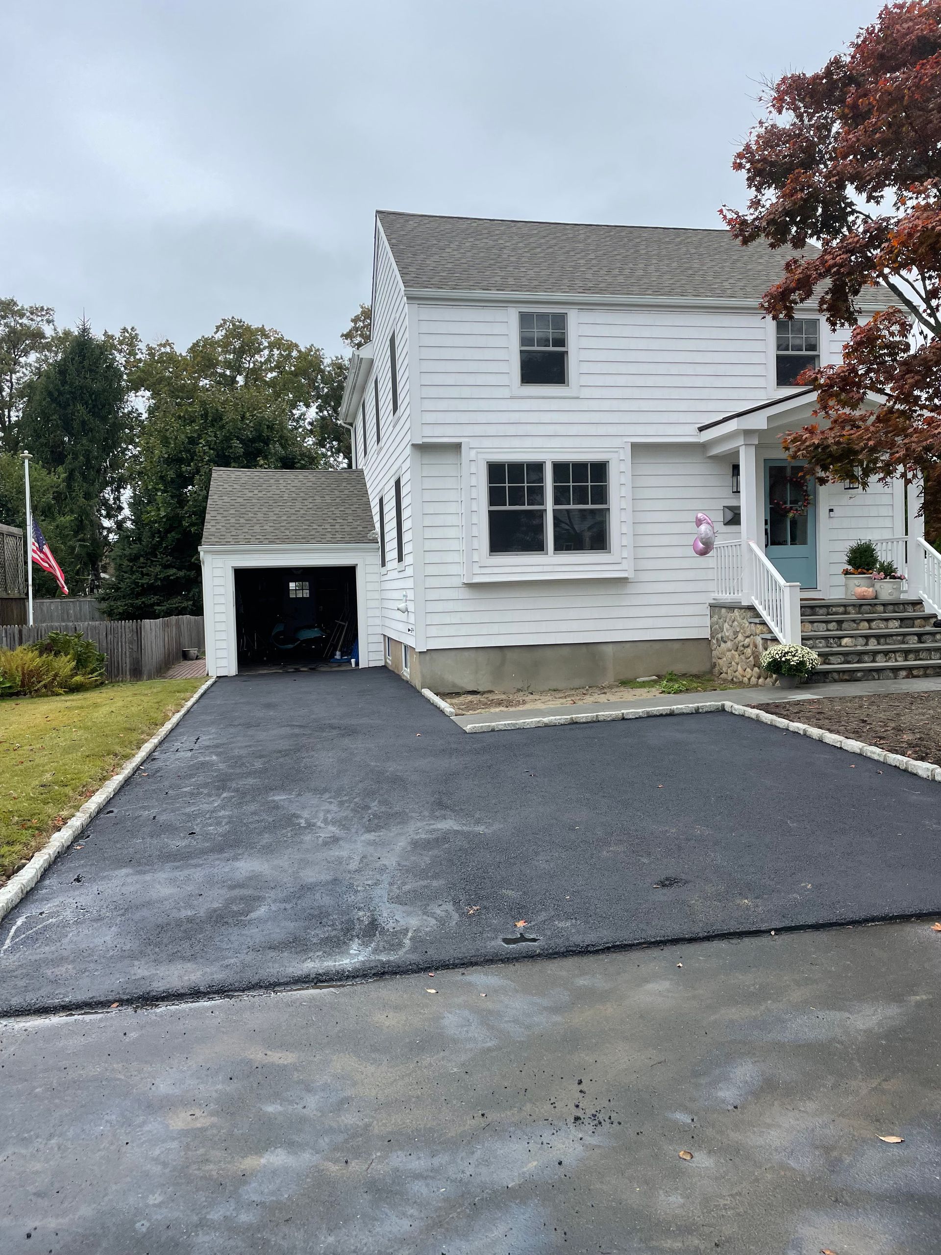 White two-story house with a black gravel driveway and detached garage on an overcast day