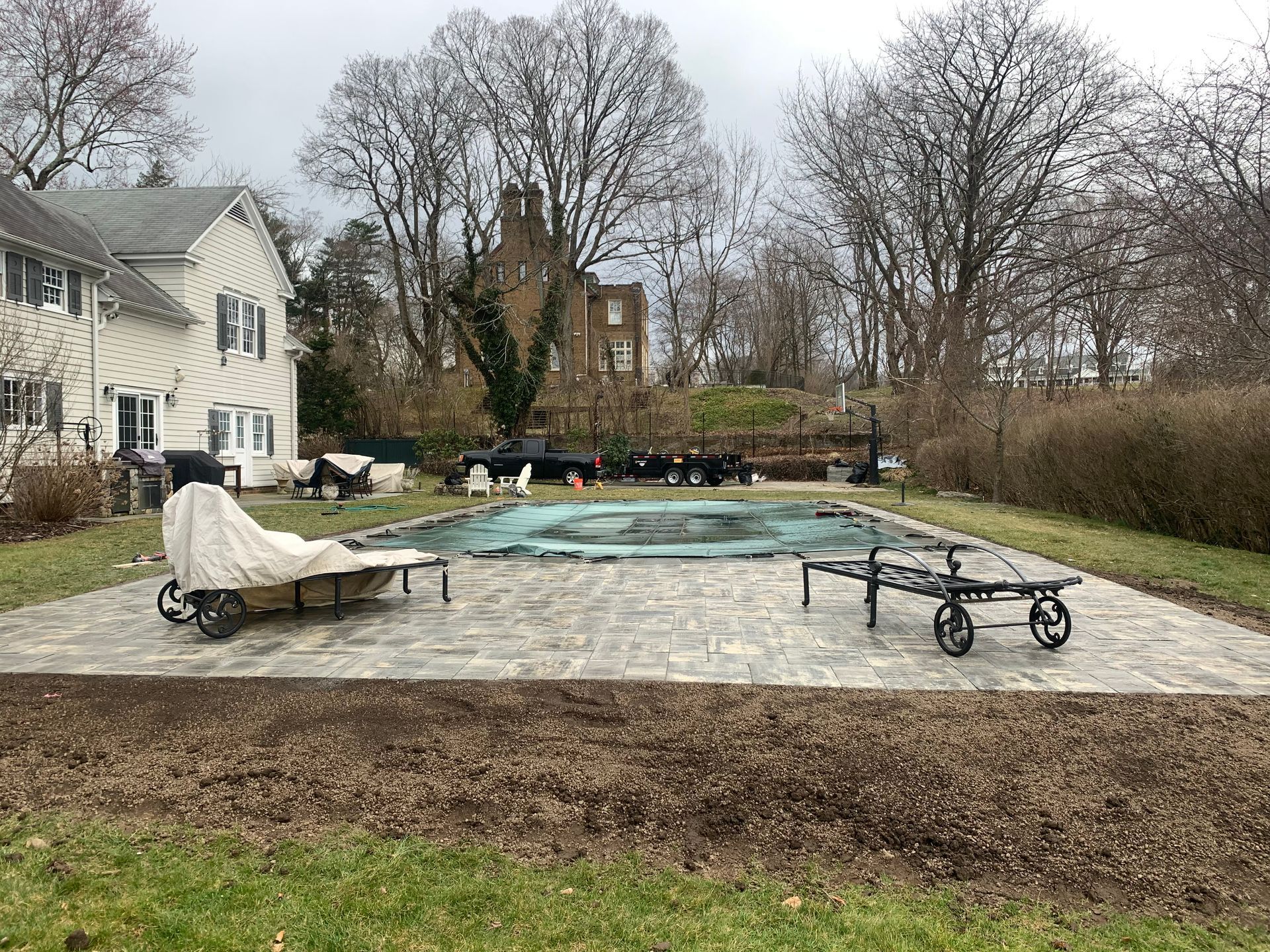 Covered backyard pool with patio furniture beside a house on a cloudy day