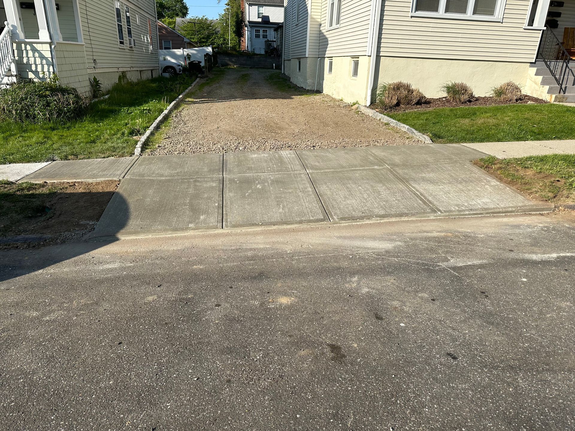 Driveway and gravel path between two houses, with a concrete sidewalk in front.