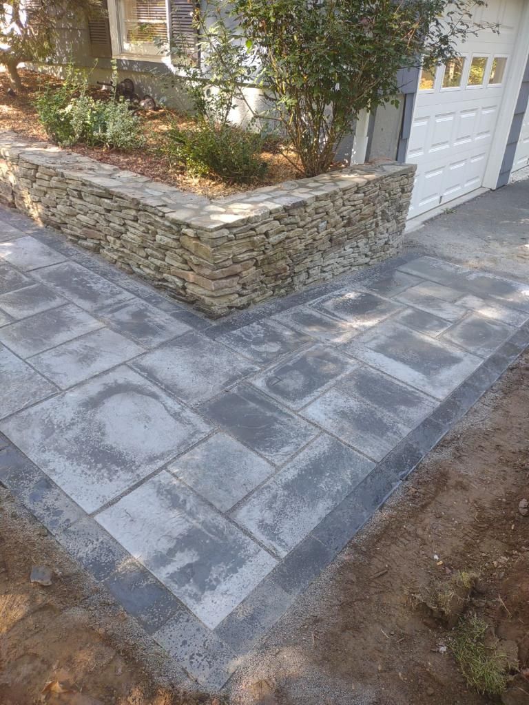 Stamped concrete patio beside a stone planter wall and white garage door