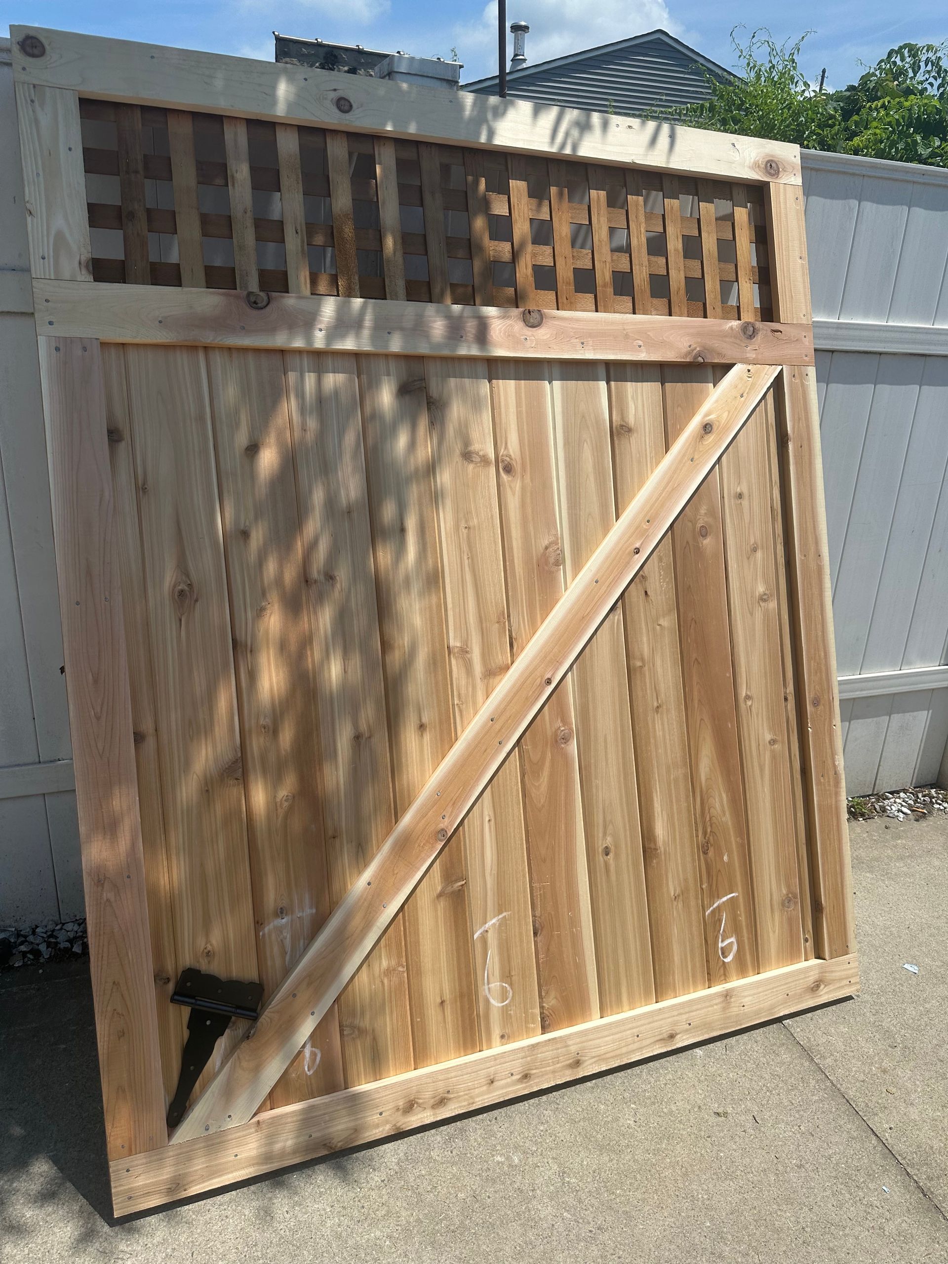 Wooden outdoor gate with diagonal brace, sunlight casting shadows, leaning against a wall