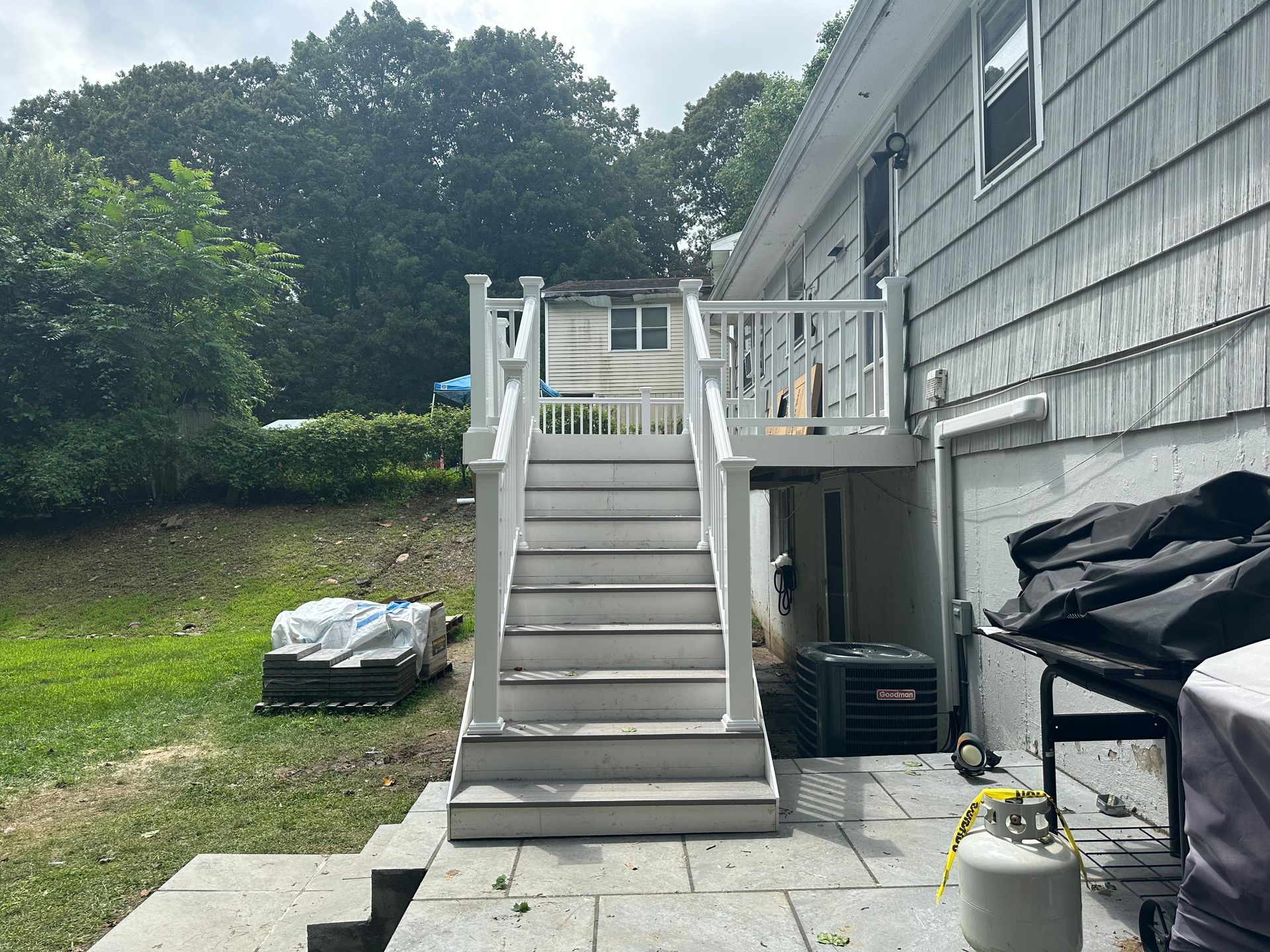 Outdoor staircase beside a gray house, with a small deck, lawn, and covered items below the steps