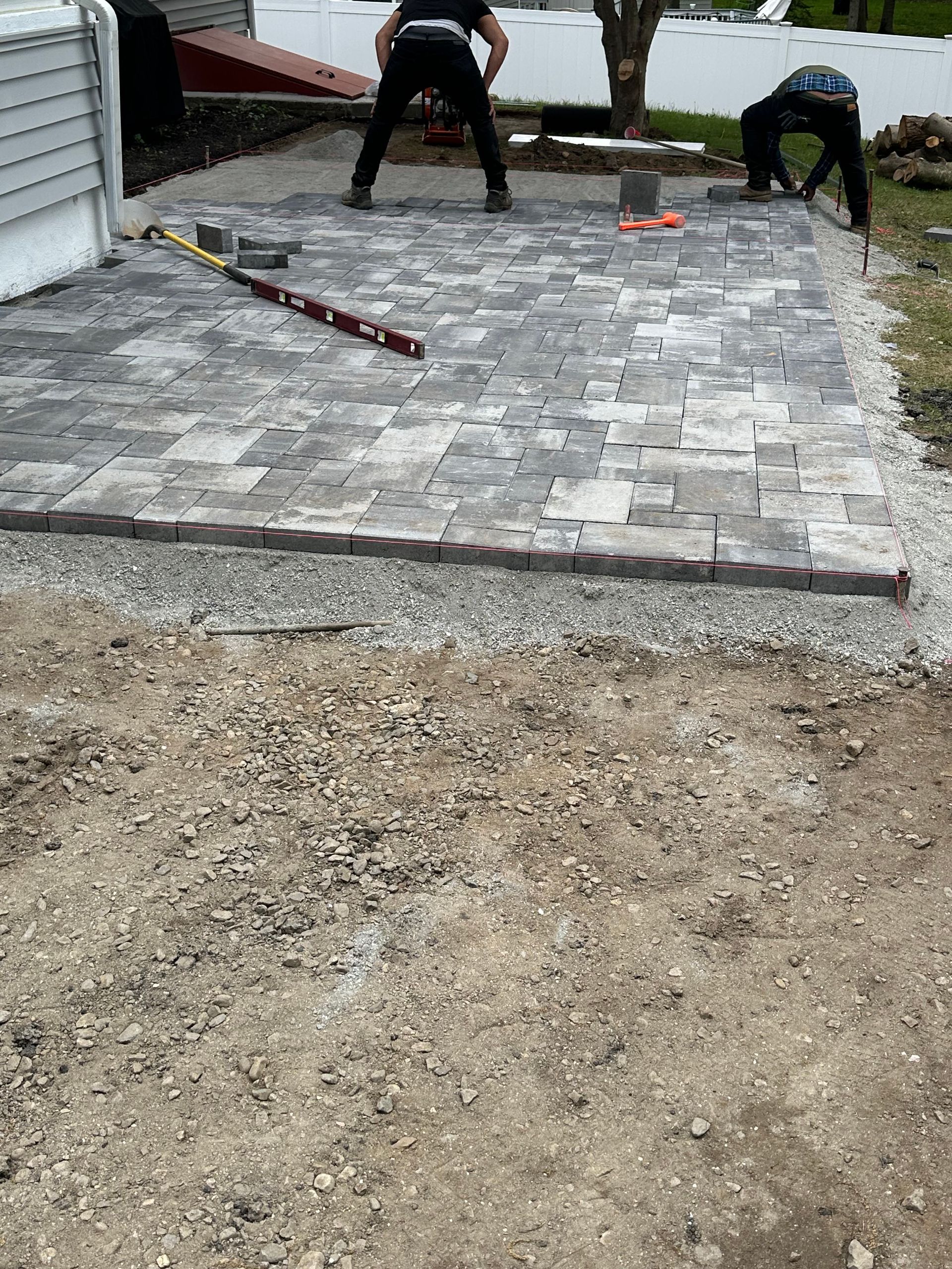 Two workers laying gray paver stones in a driveway beside a house
