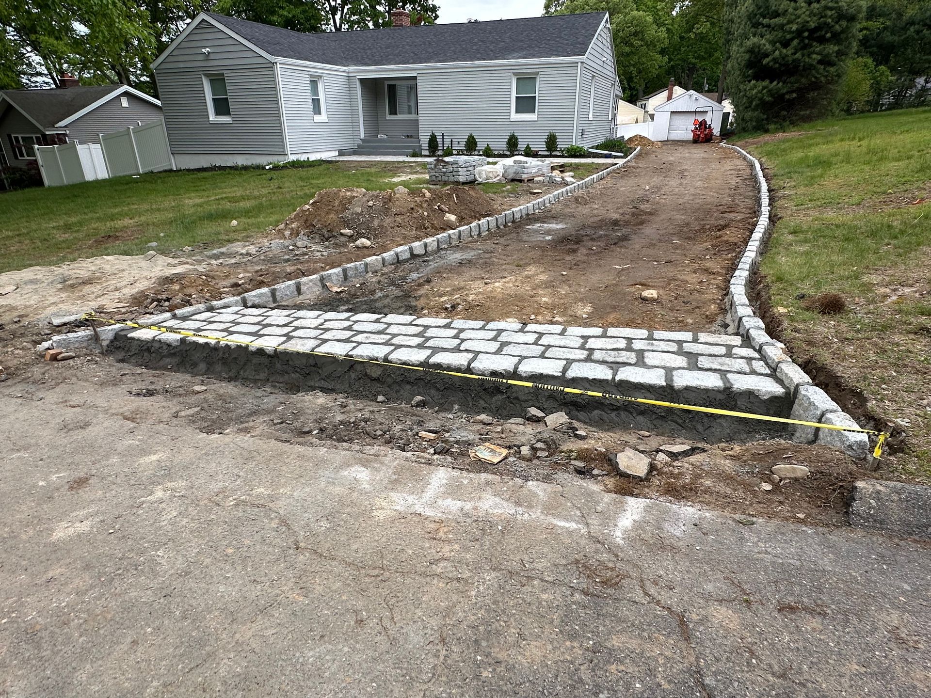 New stone-bordered driveway apron beside a gray house with bare dirt landscaping