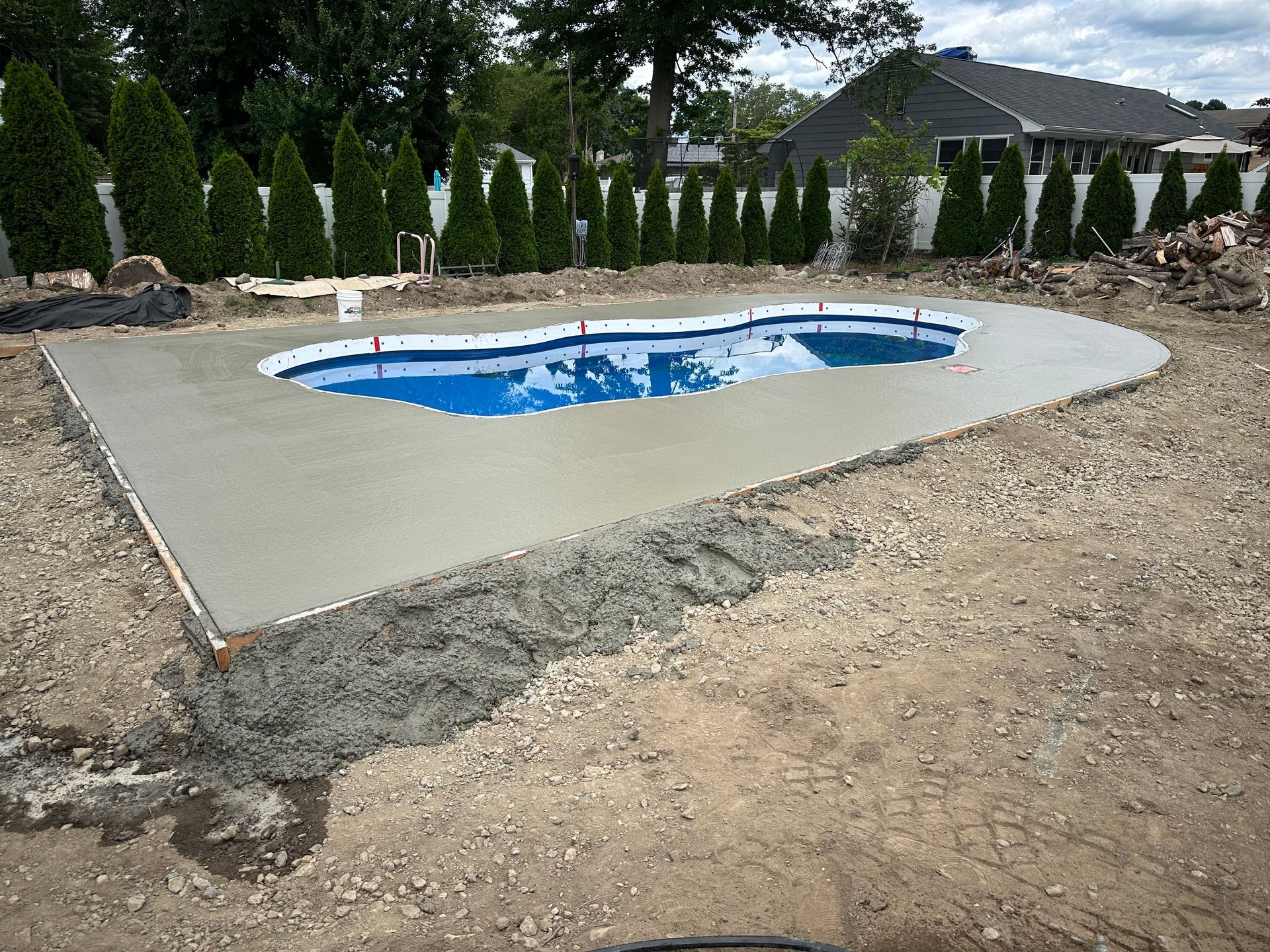 Newly poured concrete deck around a blue in-ground backyard pool under construction