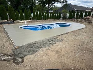 Backyard swimming pool with blue water, set in a newly poured concrete deck and surrounded by landscaping.