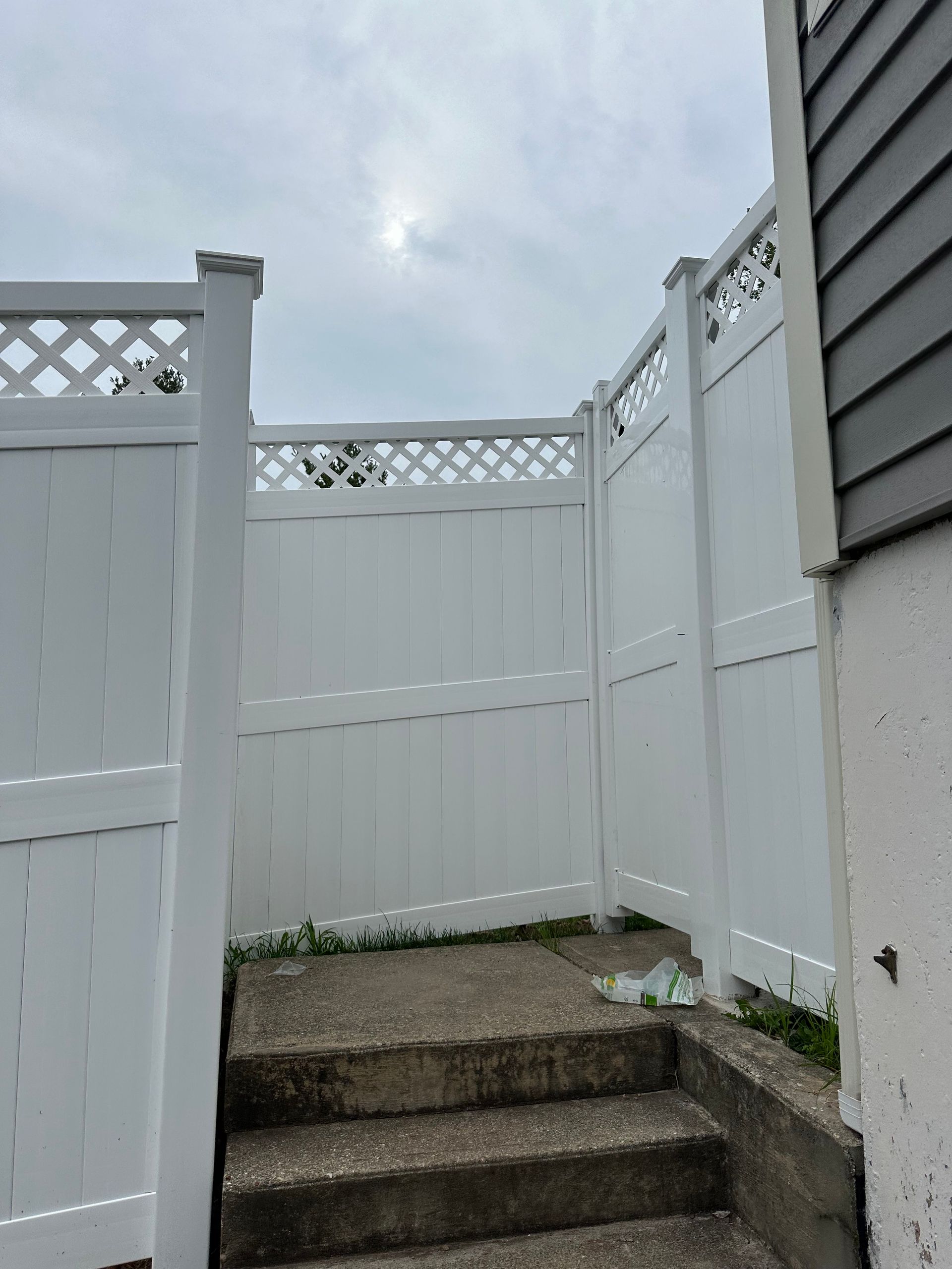 Narrow outdoor stairway with gray steps between white vinyl fences under a cloudy sky
