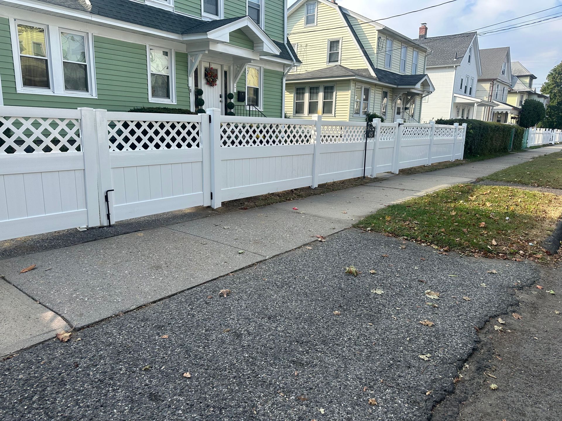 Residential street with white picket fences, green and beige houses, and a gravel sidewalk under overcast light