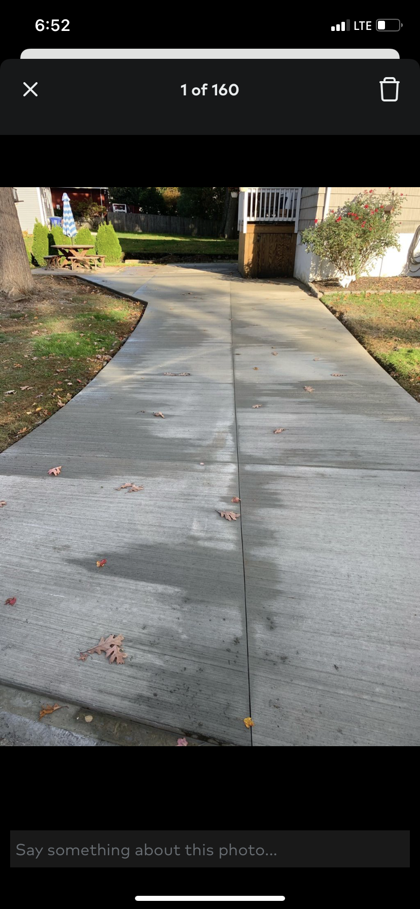 Concrete sidewalk leading to a driveway and garage beside a grassy yard with trees.