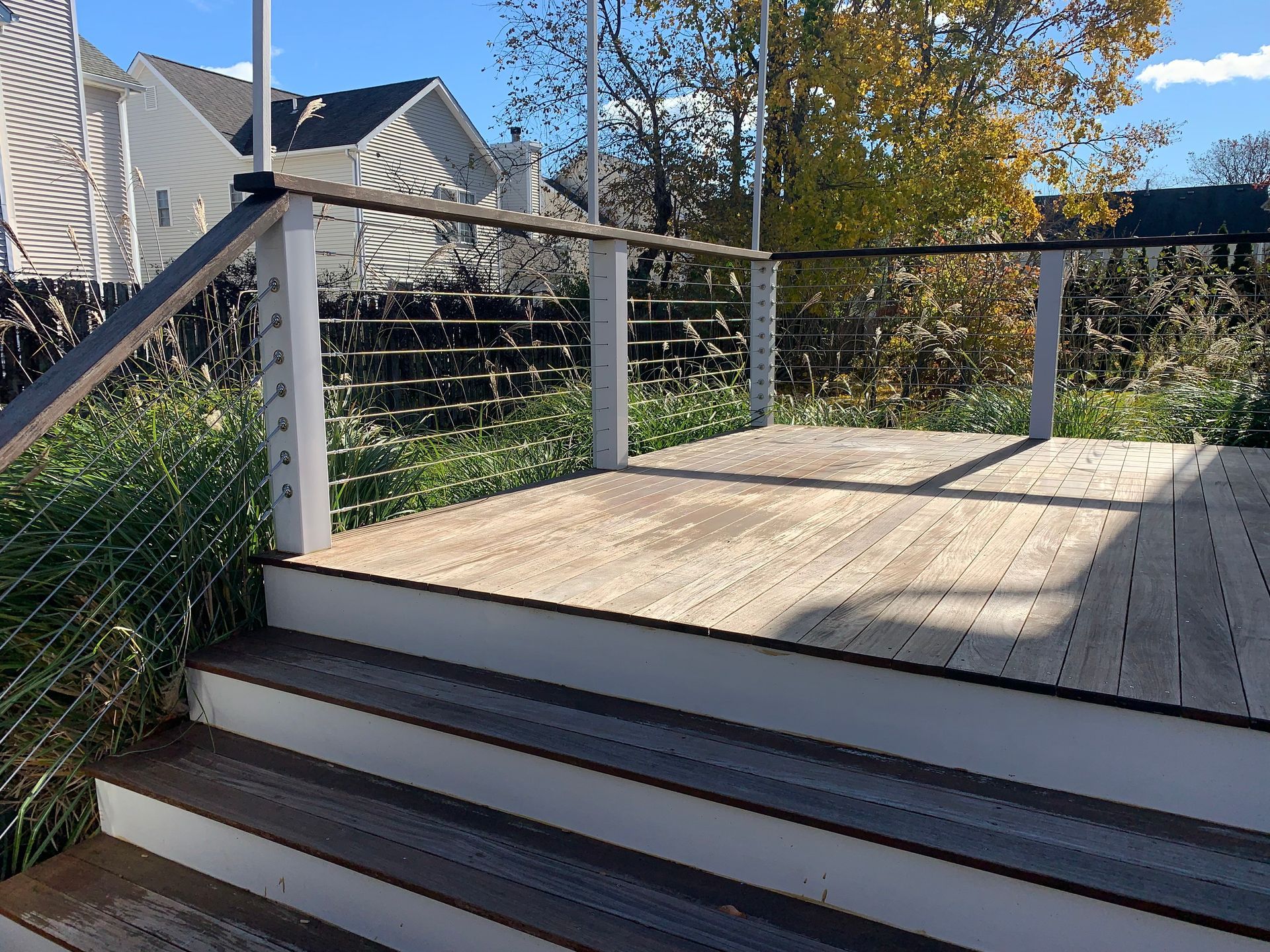 Wooden deck with steps, railing, and wire fencing overlooking a landscaped yard in autumn.