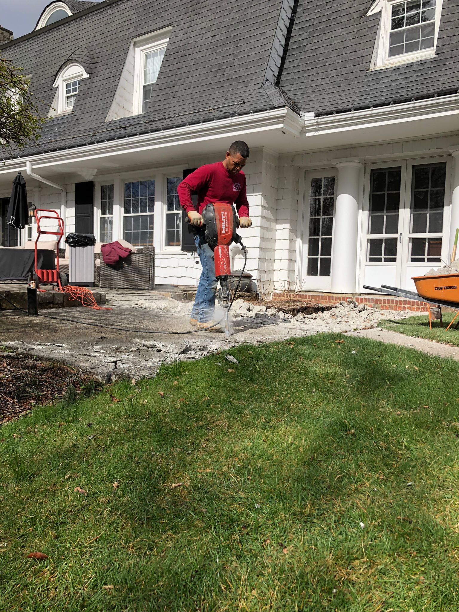 Worker using a jackhammer on a patio in front of a white house